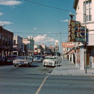 Boise Idaho historic photo. A city street filled with traffic and buildings on one side and the sky with clouds overhead. Credit: Museum of Idaho